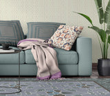 Light blue sofa with a floral pillow and purple blanket in a living room setting.