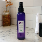Purple  spray bottle labeled 'Lavender' on a marble countertop with a tiled wall background.