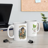 Two mugs on a desk with a laptop and plant in the background