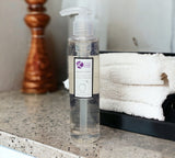 Clear bottle with pump on a bathroom counter with towels in the background