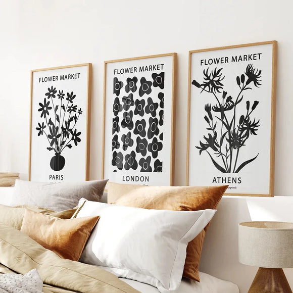 Three framed prints titled 'Flower Market' on a wall above a sofa with pillows.