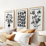 Three framed prints titled 'Flower Market' on a wall above a sofa with pillows.