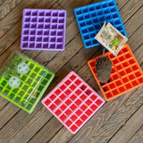 Five colorful seedling trays on a wooden surface with small plants and tools.