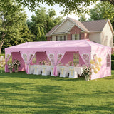 A pink event canopy tent set up on a green lawn in front of a house, decorated with white tablecloths, pink and yellow chair sashes, floral arrangements, and yellow balloons.