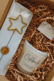 Candle labeled 'Celebrate' with a gold star-shaped candle wick trimmer on shredded brown paper