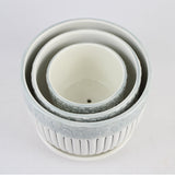 Set of three white ceramic pots with floral patterns on a light gray background