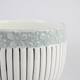 Ceramic bowl with floral pattern on rim and vertical lines on body against a white background
