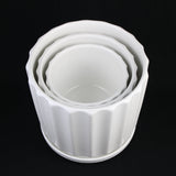 Set of white ceramic ramekins stacked on a black background 3-Piece White Ceramic Planter Pot Set with Fluted Design & Saucers