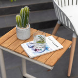 Small wooden table with a cactus, glass of water, and magazine on a patio.