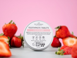 Container of toothpaste tablets with strawberries on a pink background