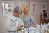 Two women standing at a table with various items, possibly in an indoor setting.