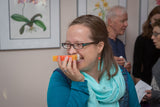 Woman holding a small object to her ear in an indoor setting with people and framed pictures in the background.