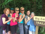 Group of women posing for a photo in front of a 'Big East Trail' sign in a forest.