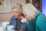 Two women looking at a container of ROSEMARY MINT ARNICA SALVE 8 oz.