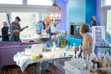 People in a room with tables displaying various items, including bottles and a TV.