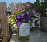 Bottle of lavender essential oil with a purple ribbon in front of flowers