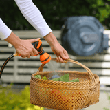 Person watering plants in a woven basket with a garden hose.