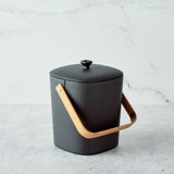 Black Astrik Compost Bin with a wooden handle on a light gray background