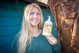 Woman holding a bottle of LEMONGRASS GOATS MILK LOTION 16 oz. or 2 oz. in front of a blue wall.