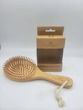 A bamboo hair brush with a natural wood handle and bristles, shown next to its brown cardboard packaging box on a light gray background.