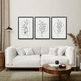 Modern living room with a white sofa, wooden coffee table, and framed Minimal Flower Line Art: Black White Wall Art Set on the wall.
