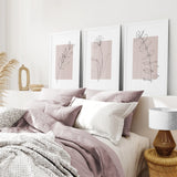 Neatly made bed with pink and white bedding, Blush Pink Botanical Line Art Print Set of 3 on the wall, and a lamp on a side table.