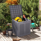 A gray plastic storage bin with its lid open, filled with garden tools and hoses, set on a wooden deck in a garden environment.