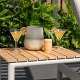 Two cocktail glasses with yellow drinks and lemon slices on a wooden table outdoors.