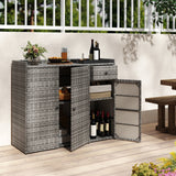 Gray wicker outdoor bar cart with two doors and open shelves, shown on a patio with wine bottles, a drink, and decor items. The cart has a woven texture and is pictured in a real environment with a railing, wooden floor, and table visible.
