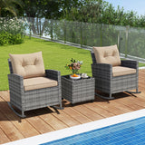 Two gray wicker outdoor rocking chairs with beige cushions and a matching small gray side table on a wooden poolside deck, with a green lawn and glass fence in the background.