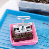 Pink seedling tray with a metal tool on a blue surface