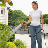 Woman watering plants with a hose in a garden setting