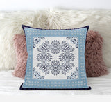 Decorative pillow with a blue border and white center featuring a black floral pattern, placed on a fluffy white and pink surface.