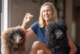 Woman holding VANILLA SWIRL LUXURY LIP BUTTER™ - THE APPALACHIAN GOAT with two dogs sitting beside her indoors.