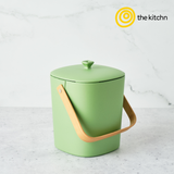 Green Astrik Compost Bin with wooden handle on a light gray background, featuring 'the kitchn' logo.