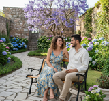 Couple sitting on a bench in a garden with flowers and stone walls.