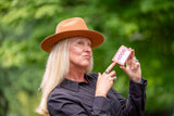 Person wearing a brown hat holding a card with 'GOOD' on it against a green blurred background