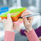 Person holding a colorful compartmentalized snack container with a marker.