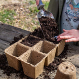 Person filling biodegradable pots with soil using a trowel. CowPots® #3 6-cell