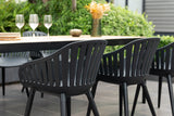 Outdoor dining setup with black chairs and a table, featuring wine glasses and a vase.