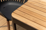 Close-up of a Portals Dark Rectangular Teak Table and 8 Nassau Black Dining Set in the background.