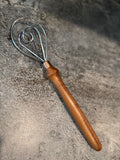 Metal whisk with wooden handle on a textured stone surface