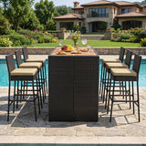 A 7-piece outdoor bar-height dining set with a rectangular wicker table and six matching barstools with beige cushions, arranged on a stone patio next to a swimming pool in front of a luxurious house.