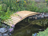 Wooden bridge over a pond with greenery and flowers around