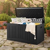 Black outdoor storage box with pillows and blankets on a stone patio