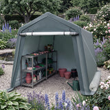 A large outdoor garden shed tent in a muted sage green color, set up in a landscaped garden with gravel flooring and gardening tools stored inside.