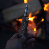 Hand holding a fire starter device with flames in the background