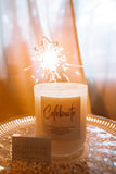 Candle with a sparkler inside on a glass table, with 'Homestead Collective' branding visible.