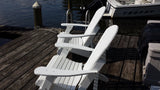 White Adirondack chairs on a wooden dock by a body of water with a boat in the background.