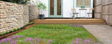 Garden with stone wall, wooden deck, and small table with chairs. Low Grow™ No-Mow Lawn Mix – Clover & Low-Maintenance Grass Alternative